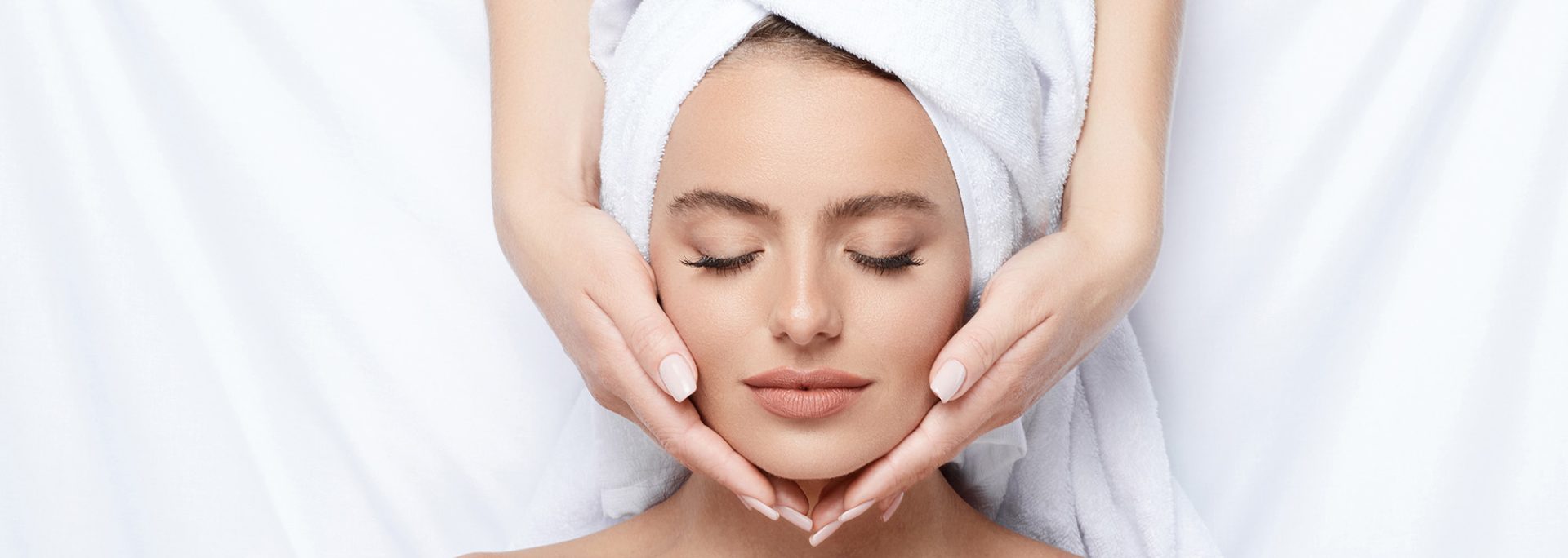 A young girl with thick eyebrows and perfect skin on a white background, a towel on her head, a beauty photo concept, skin care, a spa concept, a treatment, and a facial massage.